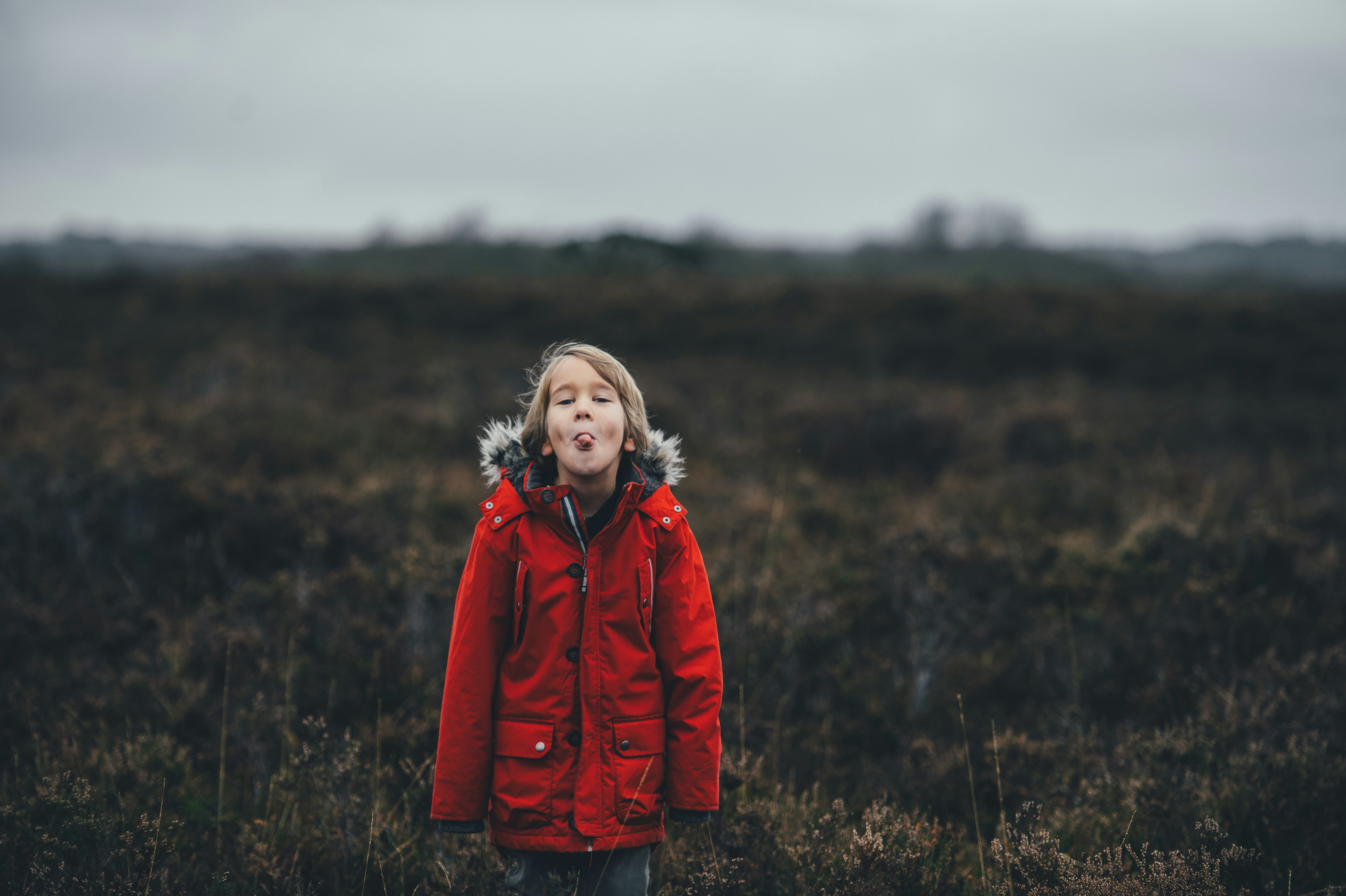 child showing tongue while standing on grass field during daytime